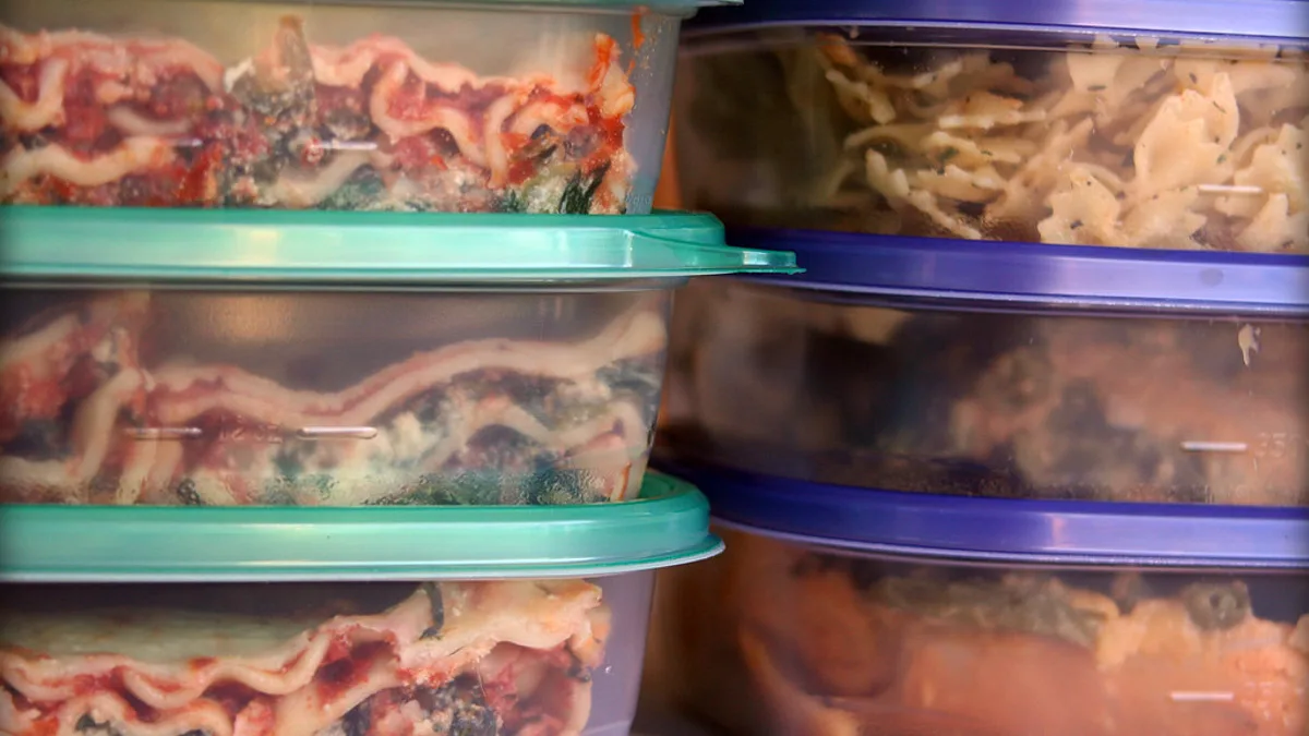 Stacked plastic containers of batch-cooked lasagna and pasta in a freezer Stacked lidded plastic containers of batch-cooked lasagna and pasta portions frozen for later shifts