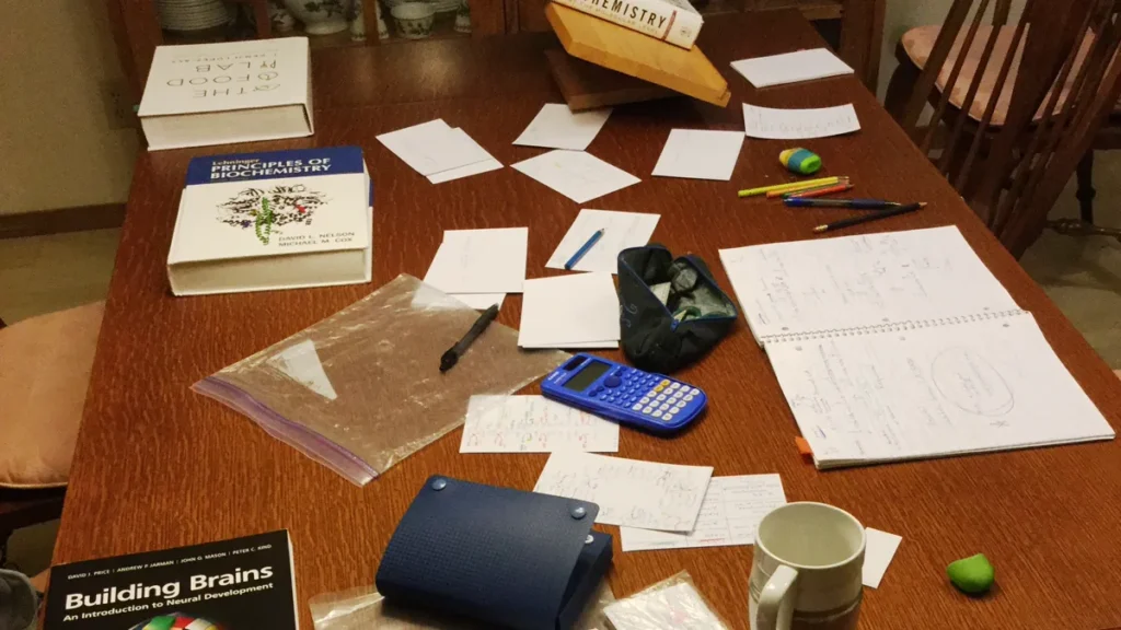 Study table covered in handwritten flash cards, textbooks, colored pencils and a mug, the setting gifts for nursing students are meant to help