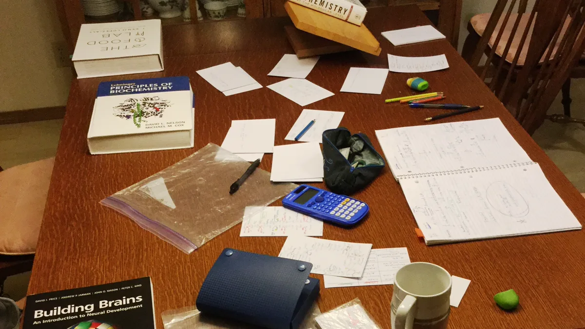 Study table covered in handwritten flash cards, textbooks, colored pencils and a mug, the setting gifts for nursing students are meant to help