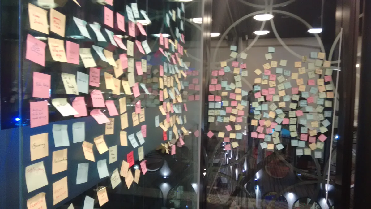 Glass wall covered in pink, yellow and blue sticky notes, the kind of gratitude board staff can add to on a break