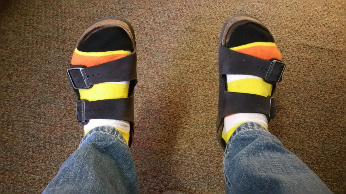 Feet in orange, yellow and white candy corn striped Halloween socks and dark sandals on a carpet