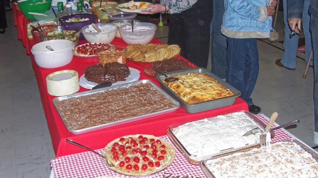 Long potluck buffet table covered with trays of casseroles, desserts and salads for a staff holiday meal