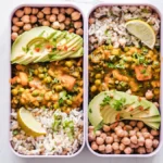 Two lidless meal prep containers filled with rice, chickpeas, vegetable curry, avocado and lemon for a nurse's shift lunch