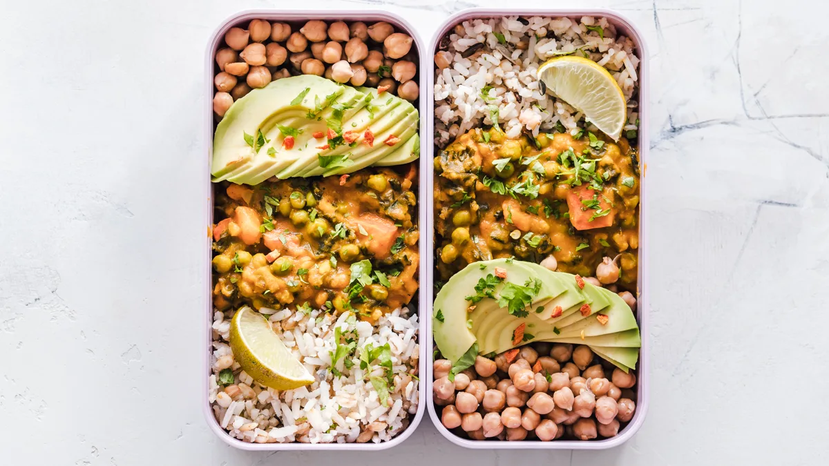 Two meal prep containers of rice, chickpea curry and avocado packed for a shift Two lidless meal prep containers filled with rice, chickpeas, vegetable curry, avocado and lemon for a nurse's shift lunch