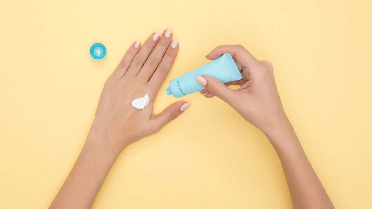 Person squeezing hand cream from a blue tube onto the back of one hand, a simple nurse gift idea