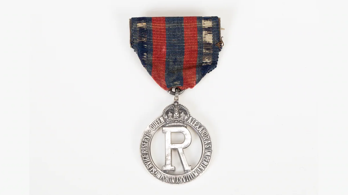 Silver nursing badge on a red and navy striped ribbon from the First World War, an early example of a nursing pin keepsake