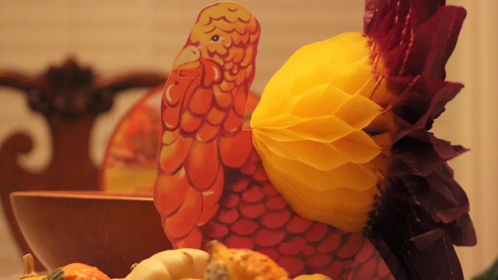 Retro paper turkey decoration with a honeycomb tail beside mini gourds, a simple Thanksgiving at work table idea